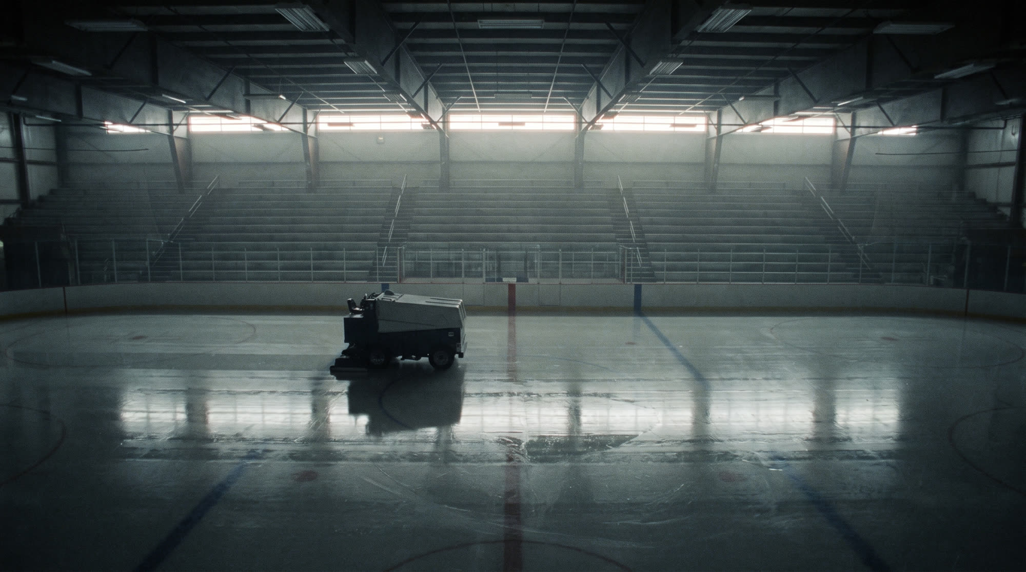 A zamboni resurfacing the ice in a dark, empty arena