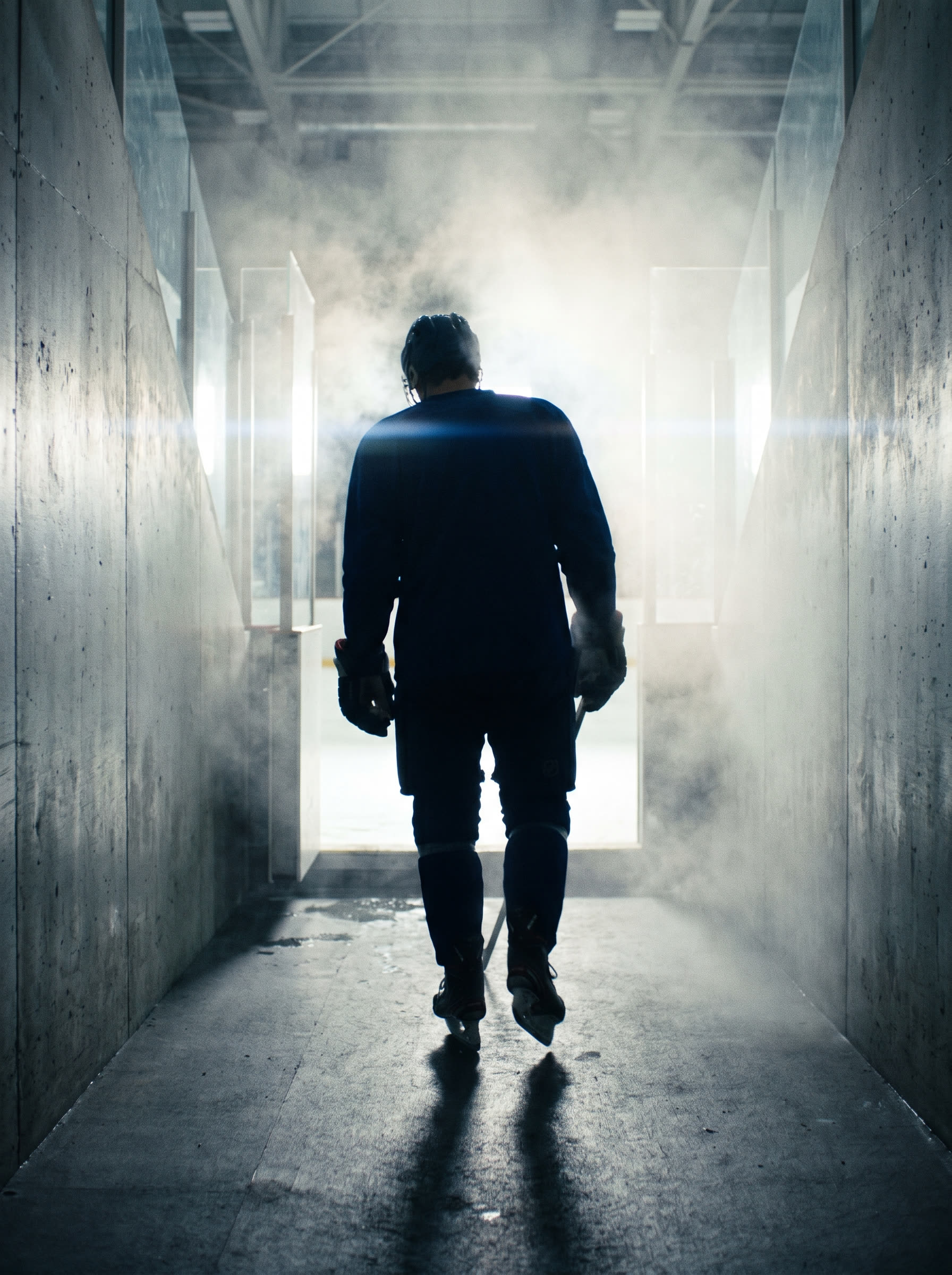 A player silhouetted in the tunnel walking out toward the ice